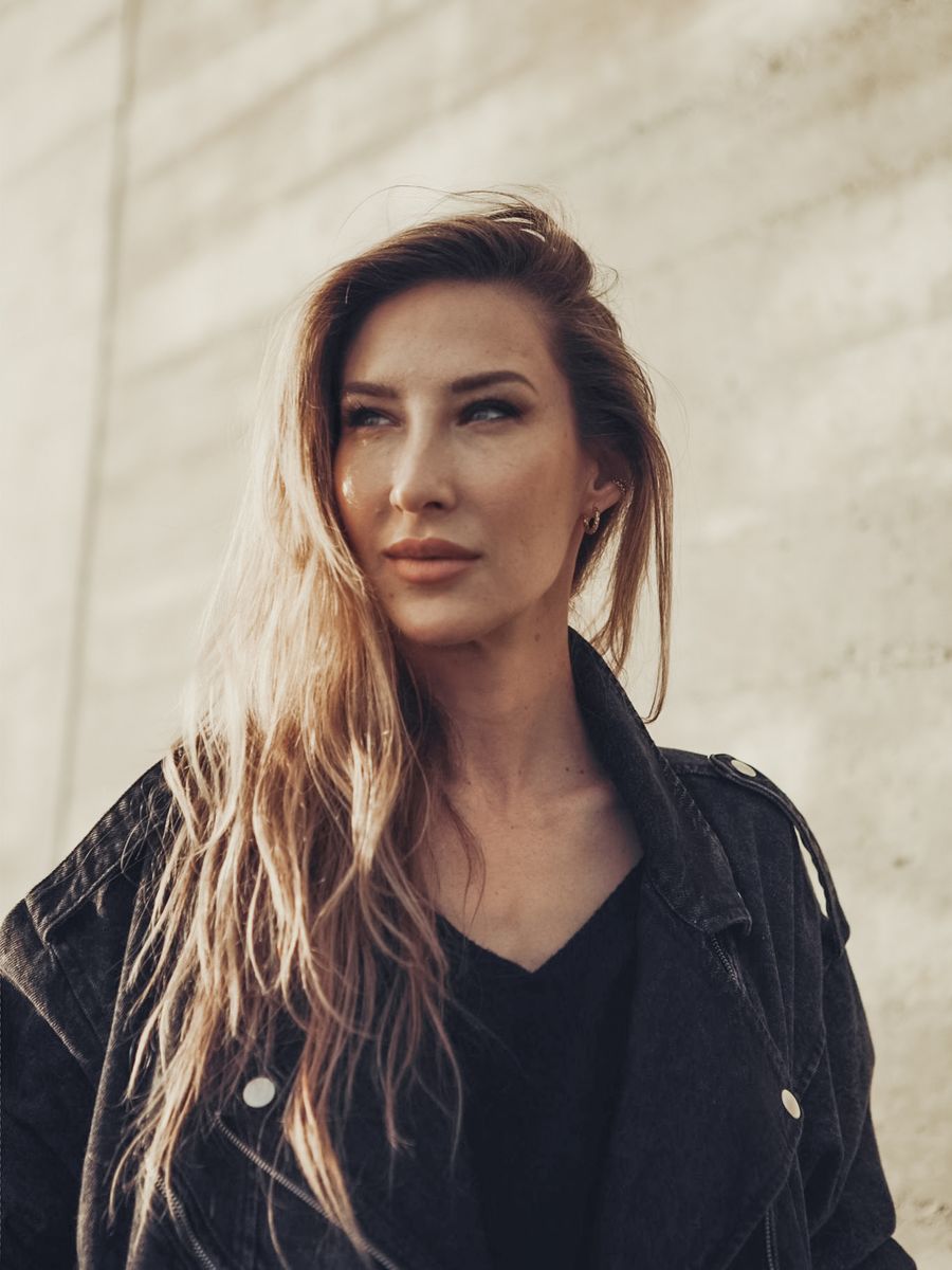 Portrait de Kristine Szabo, veste noire, devant un mur de béton clair