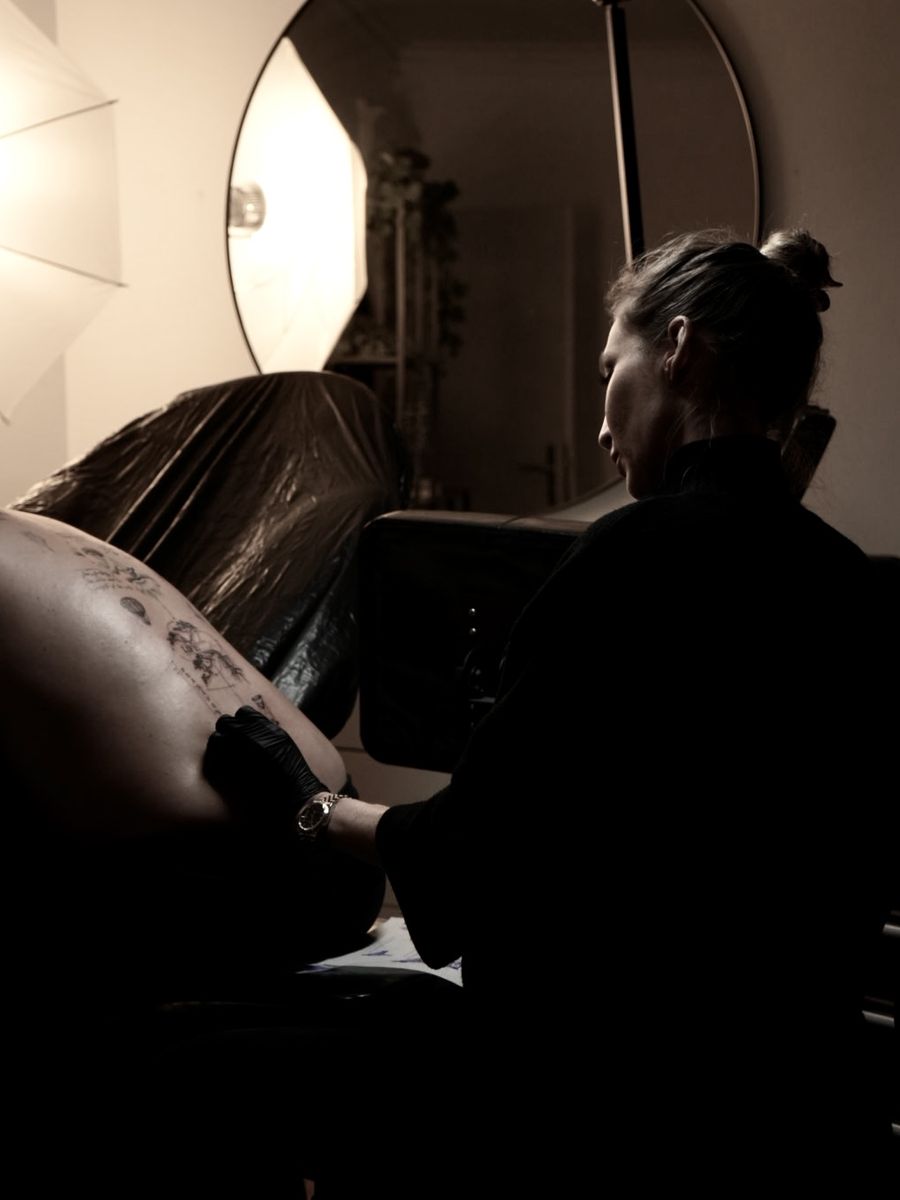 Kristine Szabo au travail dans son studio, penchée sur un dos en cours de tatouage