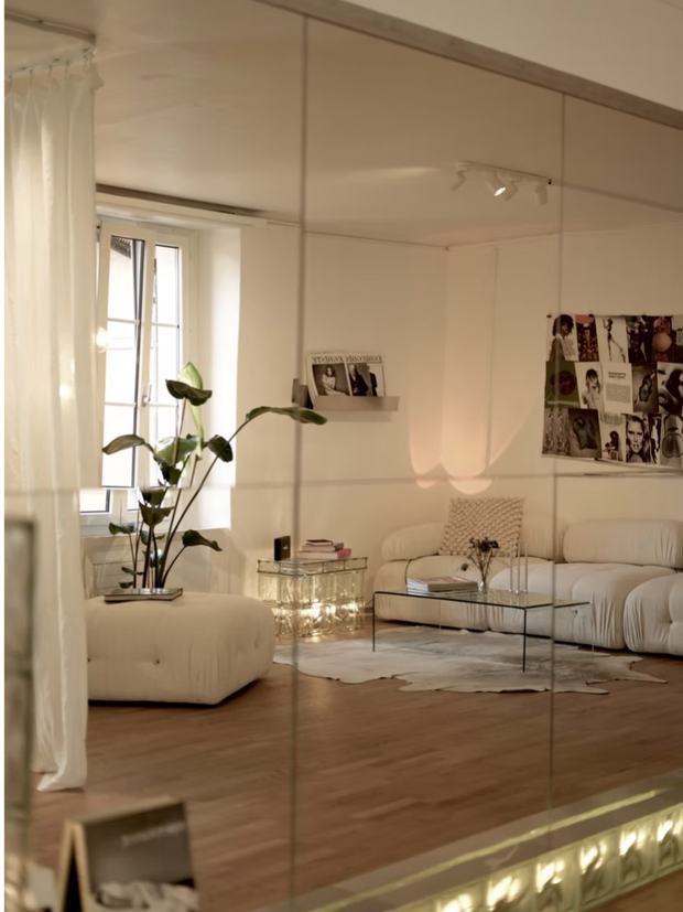 Le salon du studio vu dans le grand miroir mural, canapé clair et plante